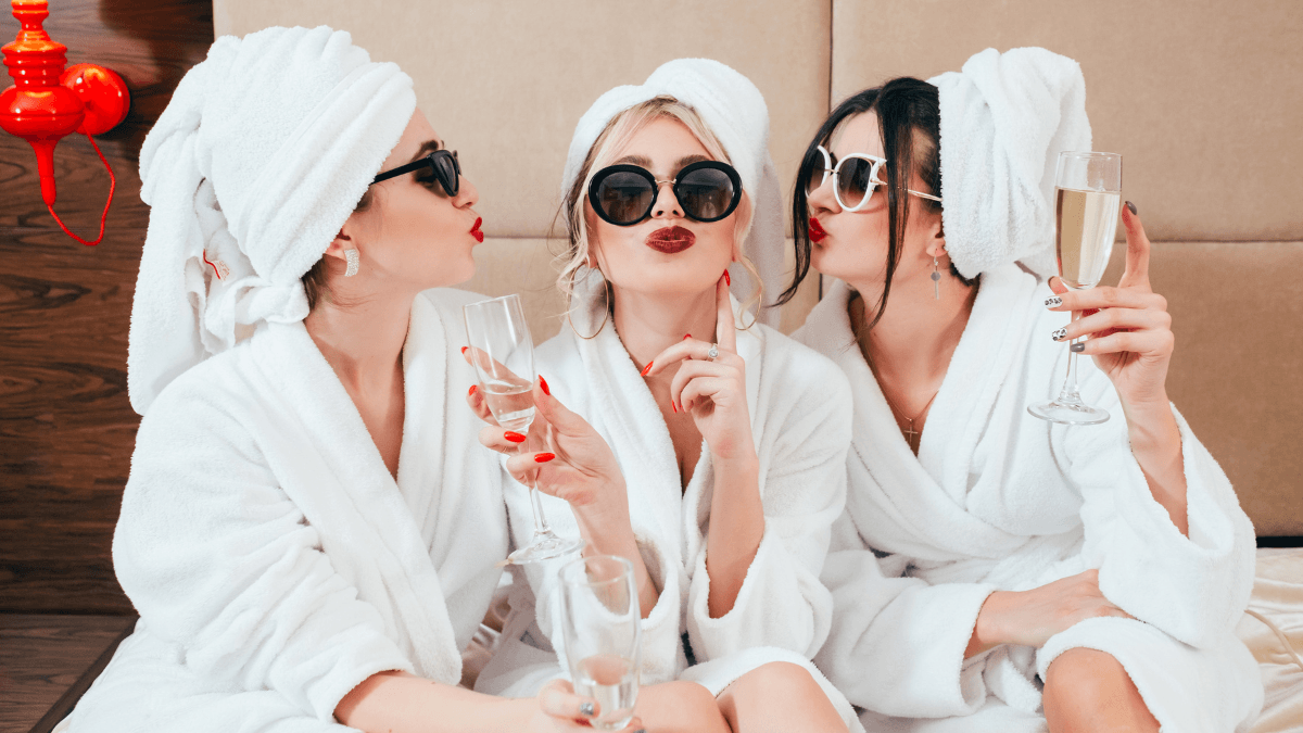 Three women in white spa robes enjoying a relaxing spa day with champagne